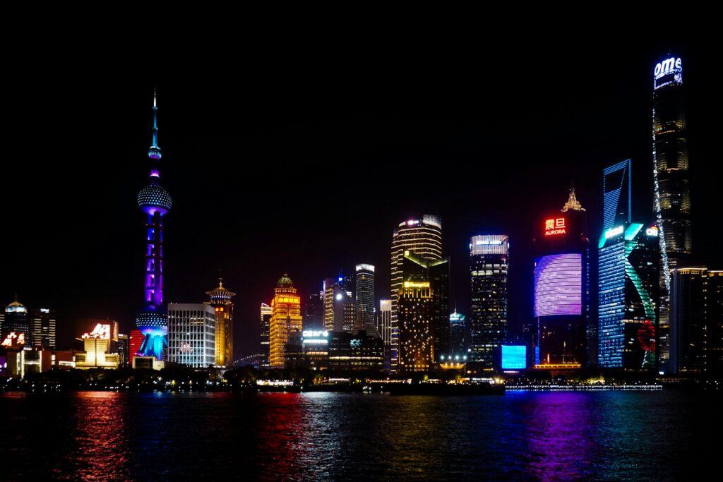 Vibrant Shanghai skyline at night featuring iconic skyscrapers and colorful lighting reflections on water.